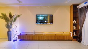 A modern living room with a flat-screen TV mounted on the wall, a wooden bench, a potted plant, and a decorative light fixture. - 1-Bedroom Apartment in Lekki off Admiralty (Lekki Phase 1)