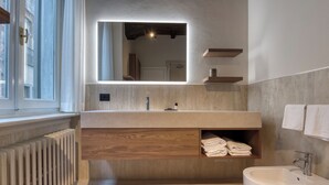 A modern bathroom with a large mirror, wooden vanity, built-in shelves, a radiator, and a freestanding bathtub. - Le Torri Suites (Bergamo)