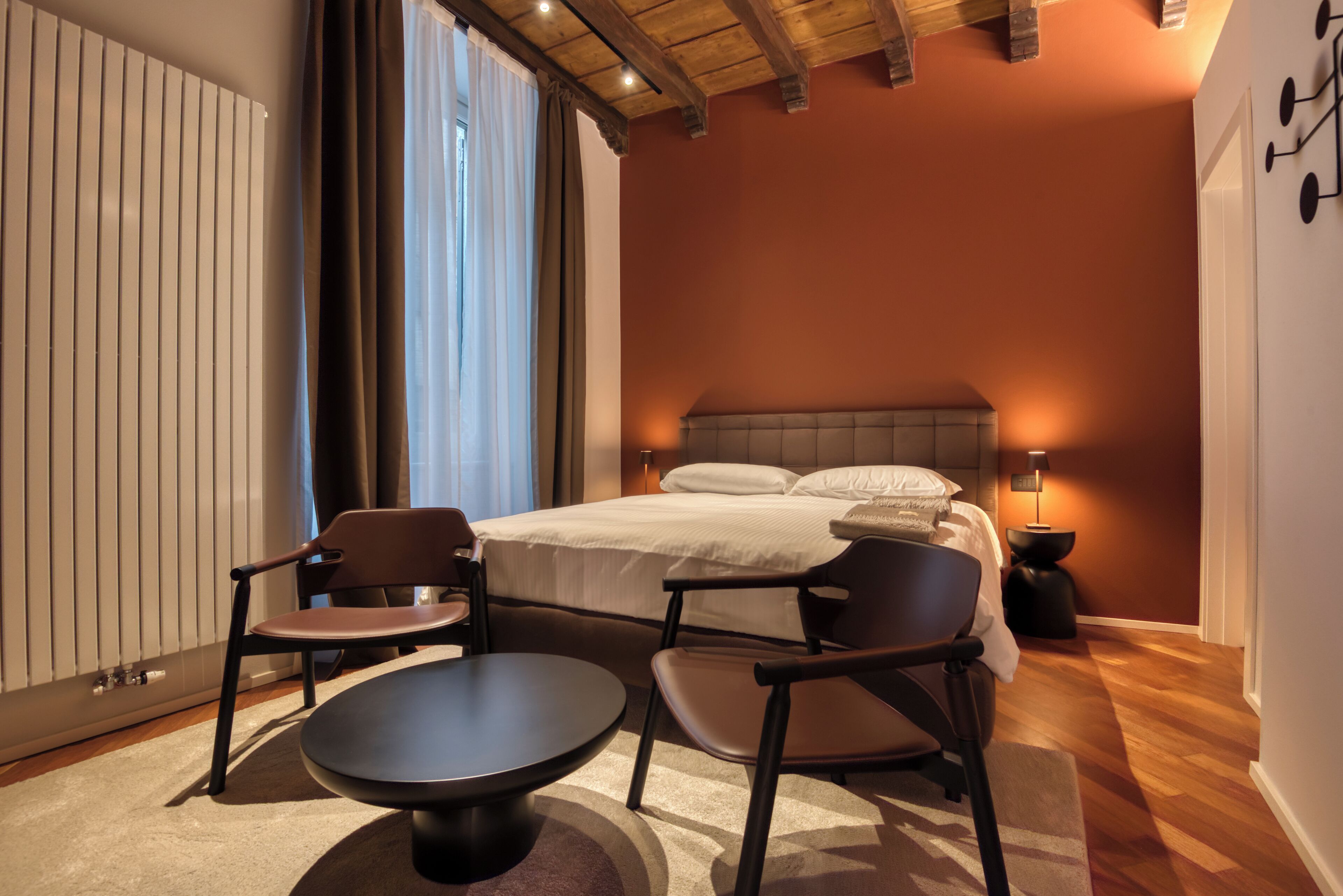 Ein Hotelzimmer mit Bett, zwei Stühlen, einem Tisch, einem Nachttisch und einem Fenster mit Vorhängen.