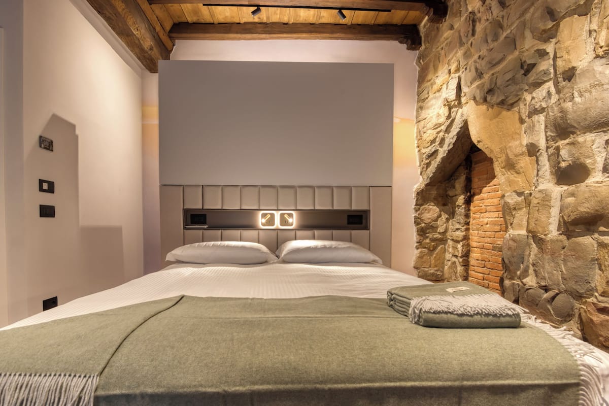 A bedroom with a stone wall, a wooden ceiling, and a modern bed with a headboard.