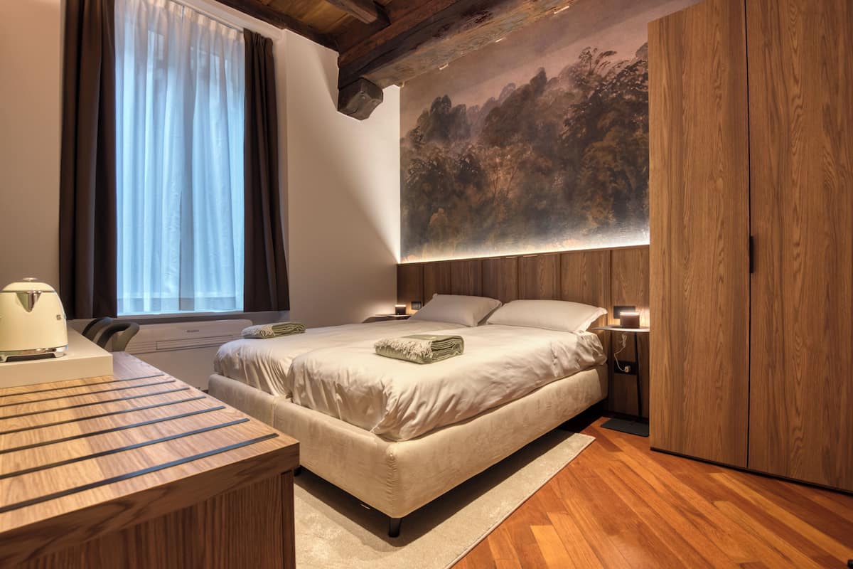 A bedroom with a bed, bedside tables, a desk, and a large painting on the wall.