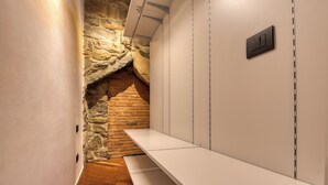 A narrow hallway with a stone wall on one side and a white panel wall on the other. There is a bench along the white wall and a light switch on the panel wall. - Le Torri Suites (Bergamo)
