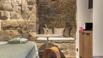 A cozy room with a stone wall, a round table with a vase, and a wooden chair.