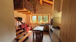 Un interior acogedor con una escalera de madera, un comedor con mesa y sillas, y una cocina con ventanal.