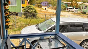 Een overdekt terras met een tafel en twee stoelen, met uitzicht op een straat met geparkeerde auto's en kleurrijke huizen.