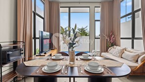A modern dining area with a large table set for four, a sofa, and a TV in the background. - Dharma Villa by Kozystay - Jimbaran (Jimbaran)