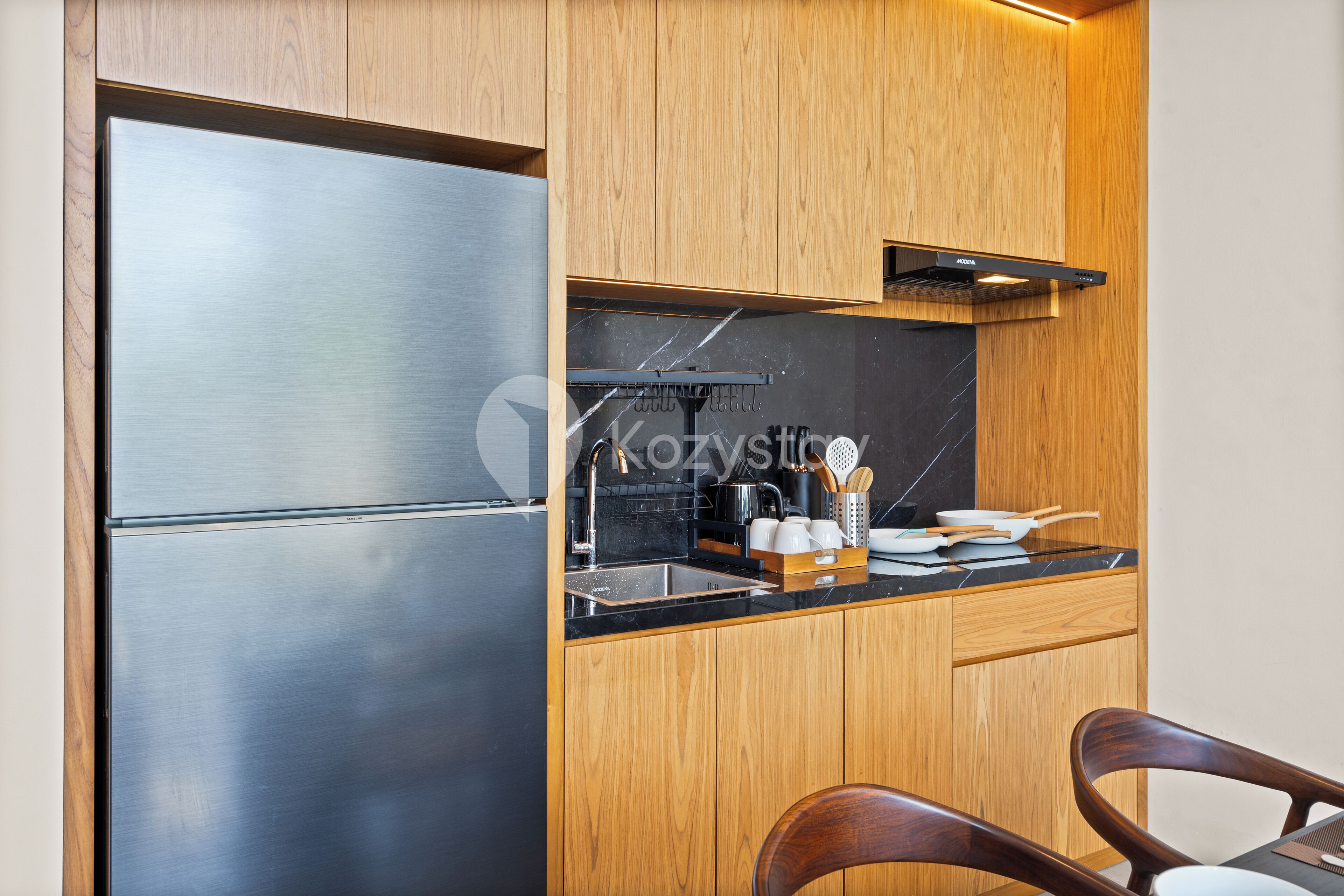 A compact kitchen with wooden cabinets, a stainless steel refrigerator, and a black countertop.