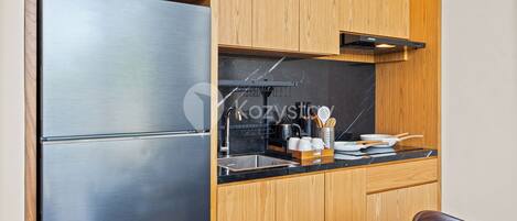 A compact kitchen with wooden cabinets, a stainless steel refrigerator, and a black countertop.