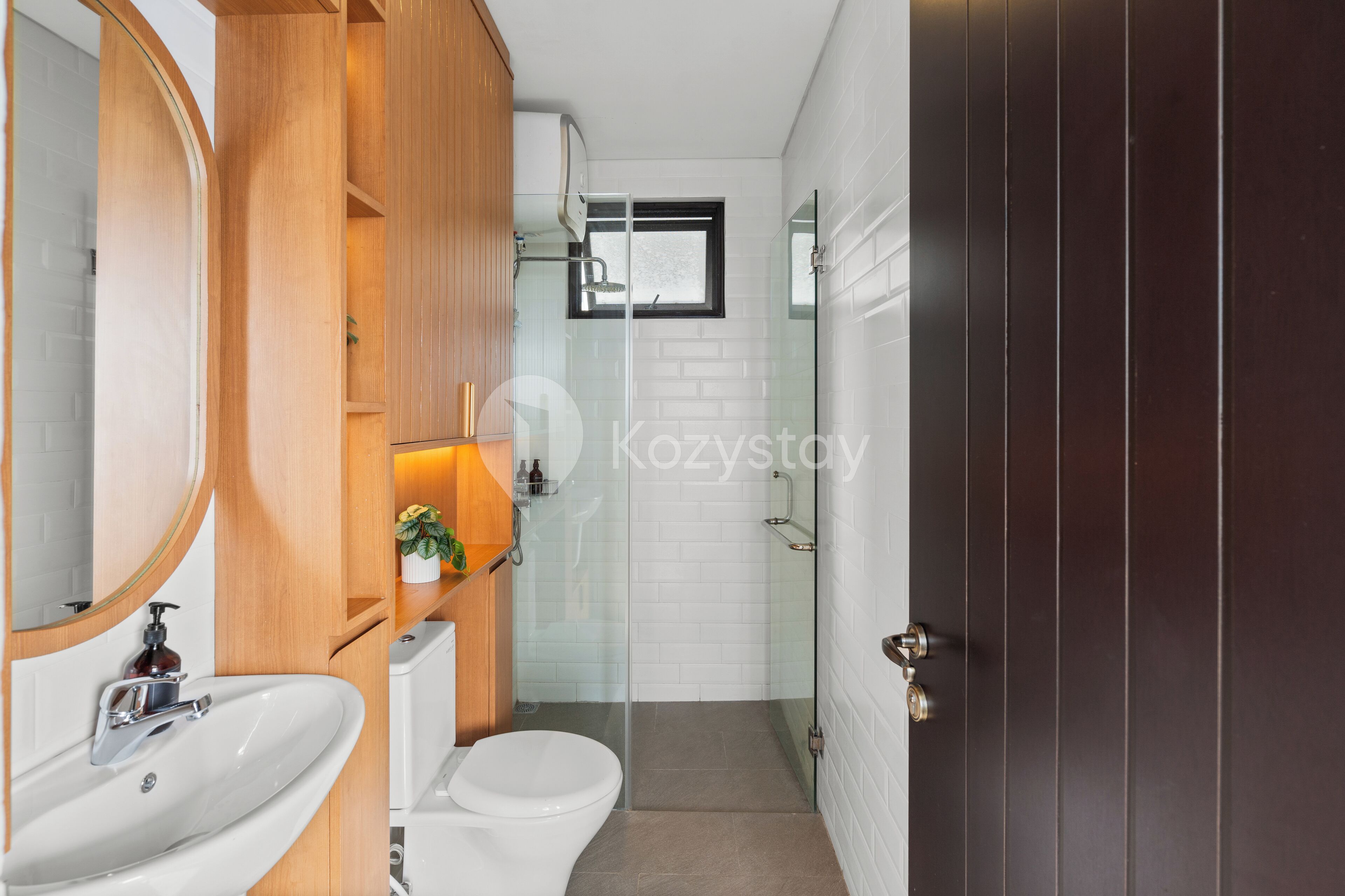 A modern bathroom with a white sink, wooden cabinets, a toilet, and a glass shower enclosure.