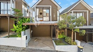 A modern residential building with a central balcony, large windows, and a well-maintained garden area. - Dharma Villa by Kozystay - Jimbaran (Jimbaran)