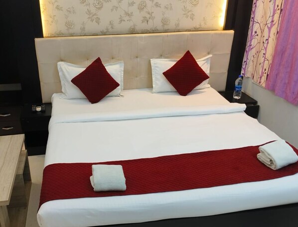 A neatly made bed with white linens and red accents, a headboard with a floral pattern, and a water bottle on the nightstand. - Hotel Shanti niketan by Nexottel (Deoghar)