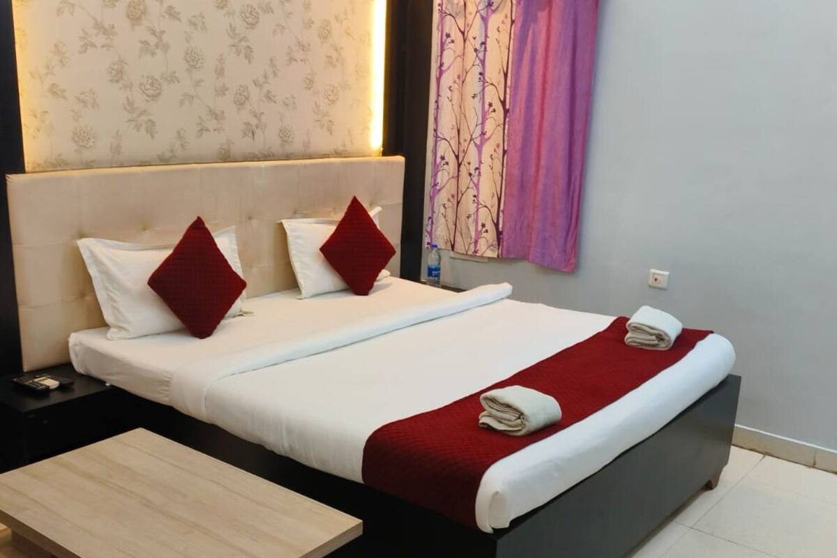 A neatly made bed with white and red bedding, a small bedside table, and a wooden nightstand.