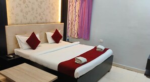 A neatly made bed with white and red bedding, a small bedside table, and a wooden nightstand. - Hotel Shanti niketan by Nexottel (Deoghar)
