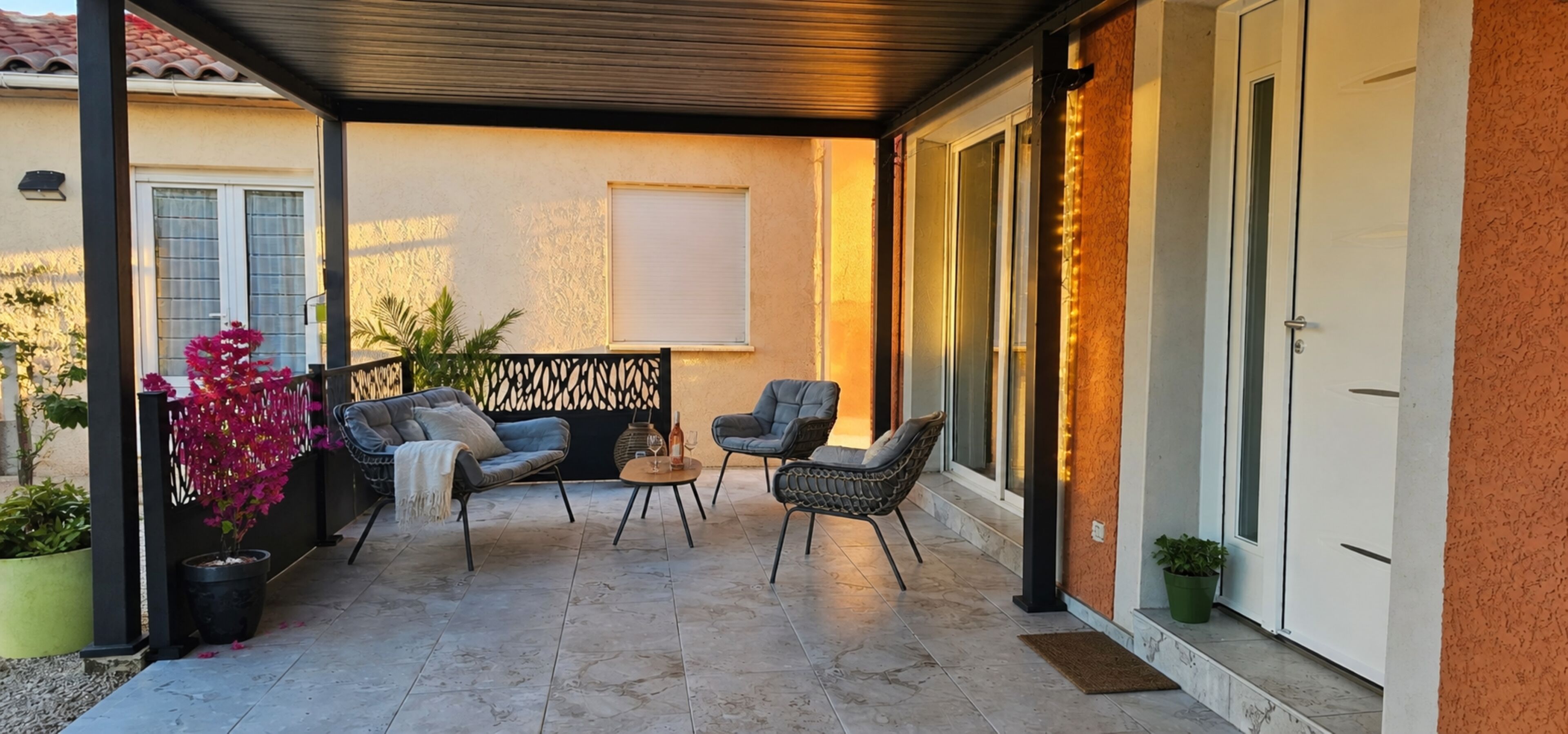 A covered patio with two chairs, a small table, and a decorative wall.