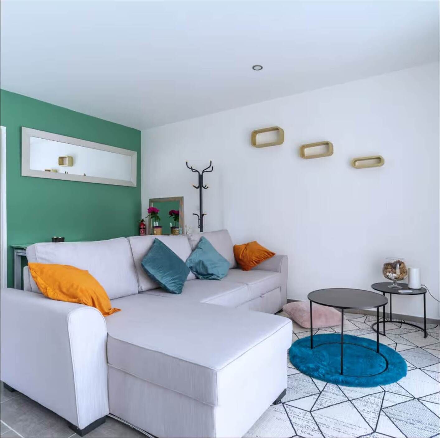 Ein modernes Wohnzimmer mit einem weißen Sofa, bunten Kissen, einem runden Couchtisch und einem blauen Teppich.