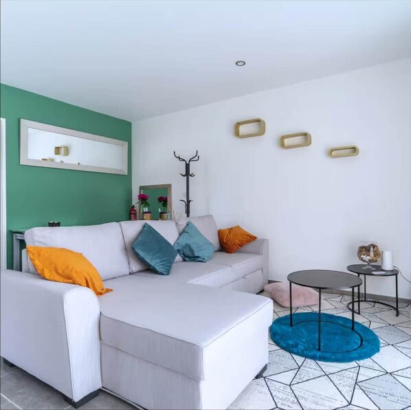 Un salon moderne avec un canapé blanc, des coussins colorés, une table basse ronde et un tapis bleu.
