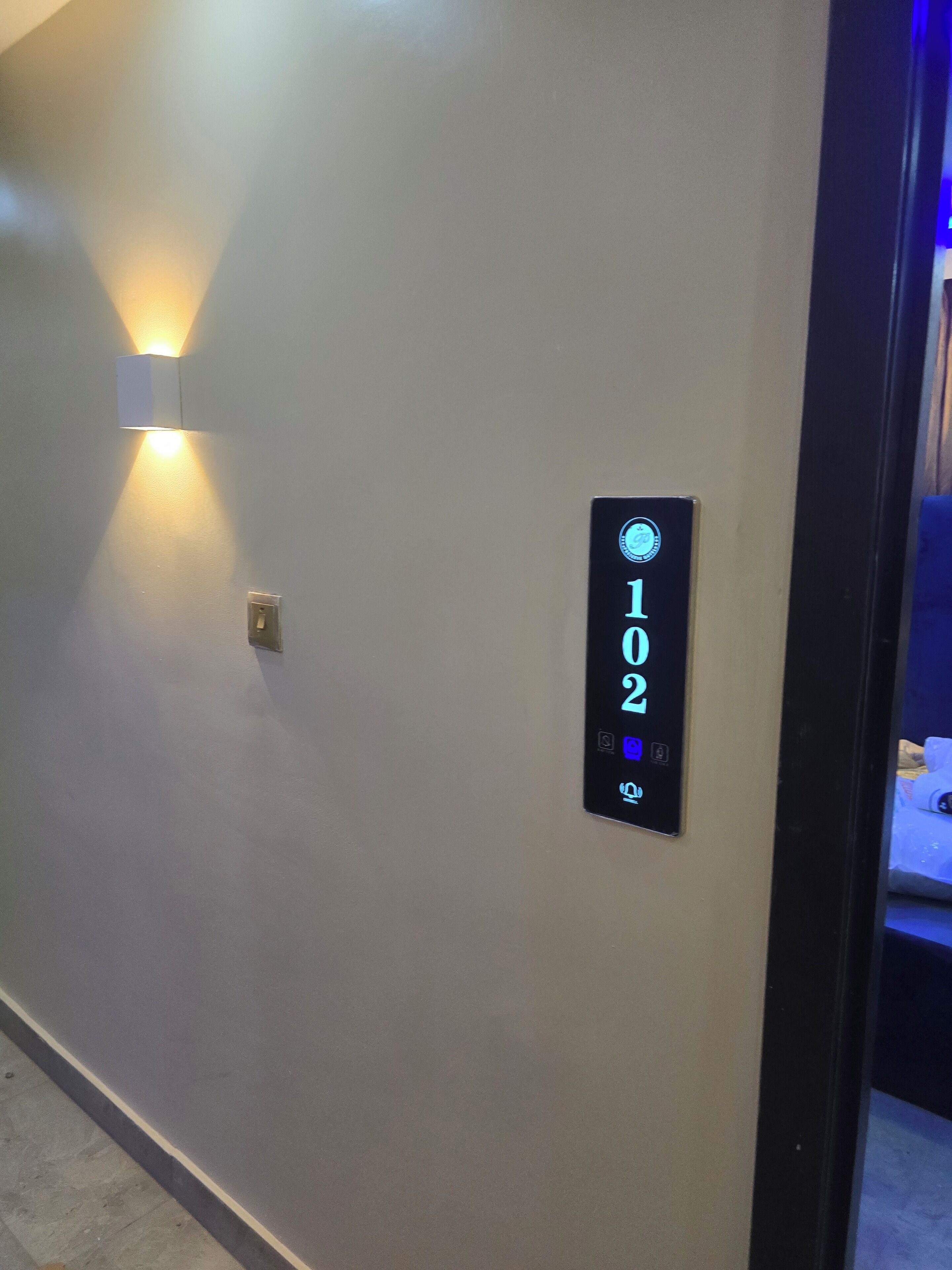 Un écran numérique fixé au mur, affichant le numéro 102 (numéro de la pièce), et un luminaire placé au-dessus.