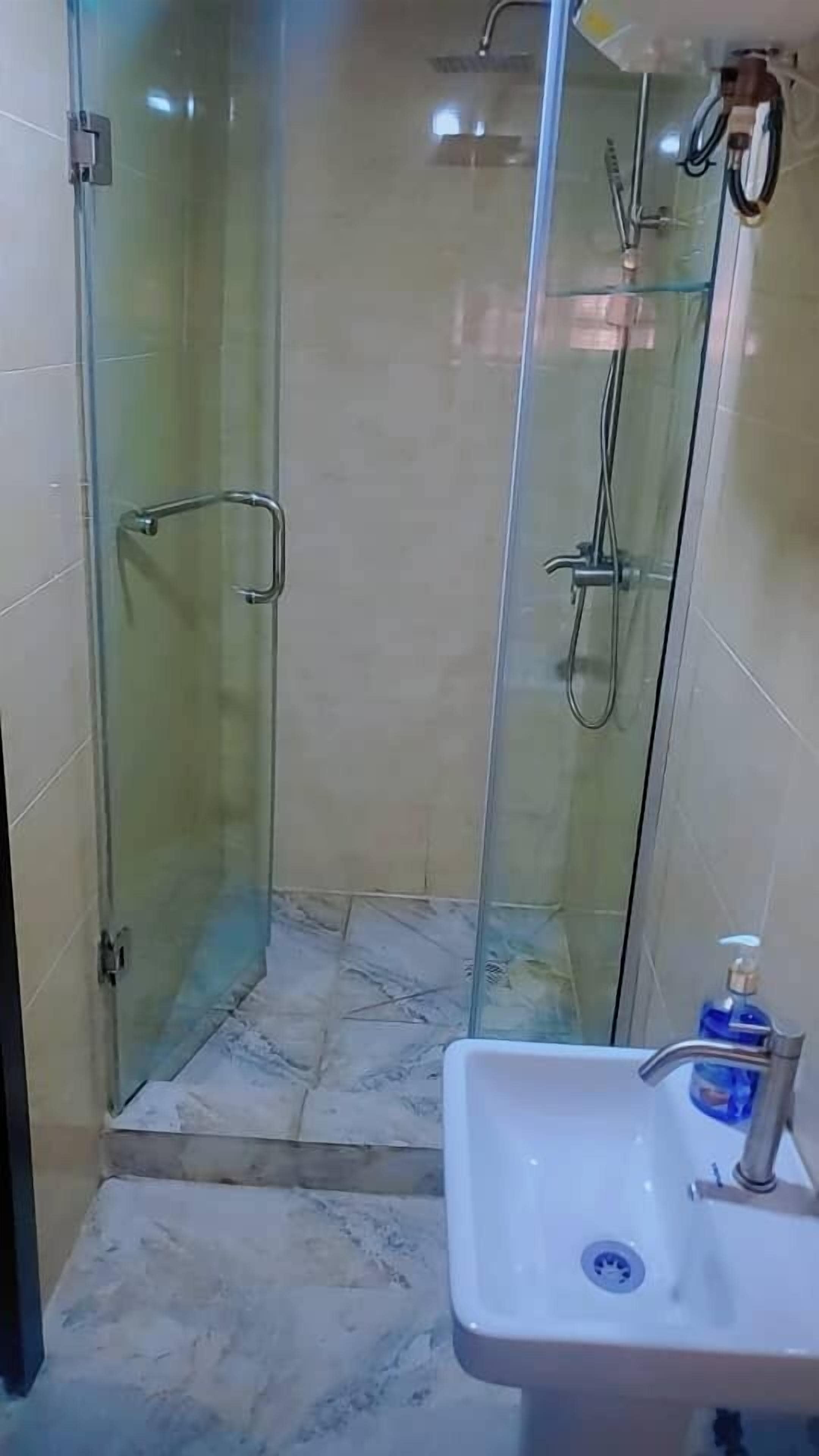 A glass-enclosed shower with a handheld showerhead, a handheld showerhead, and a wall-mounted faucet.