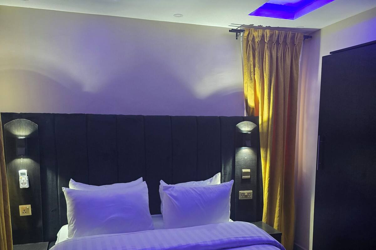 A hotel room with a large bed, two bedside tables, a headboard, and a ceiling light fixture.