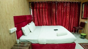 Une chambre avec un lit simple, une tête de lit rouge, du linge de lit blanc, une table de chevet avec une lampe et une poubelle verte.