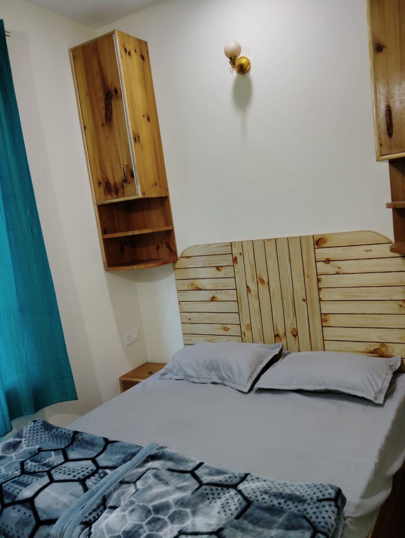 A bedroom with a wooden headboard, a bed with two pillows, and a blue patterned blanket.