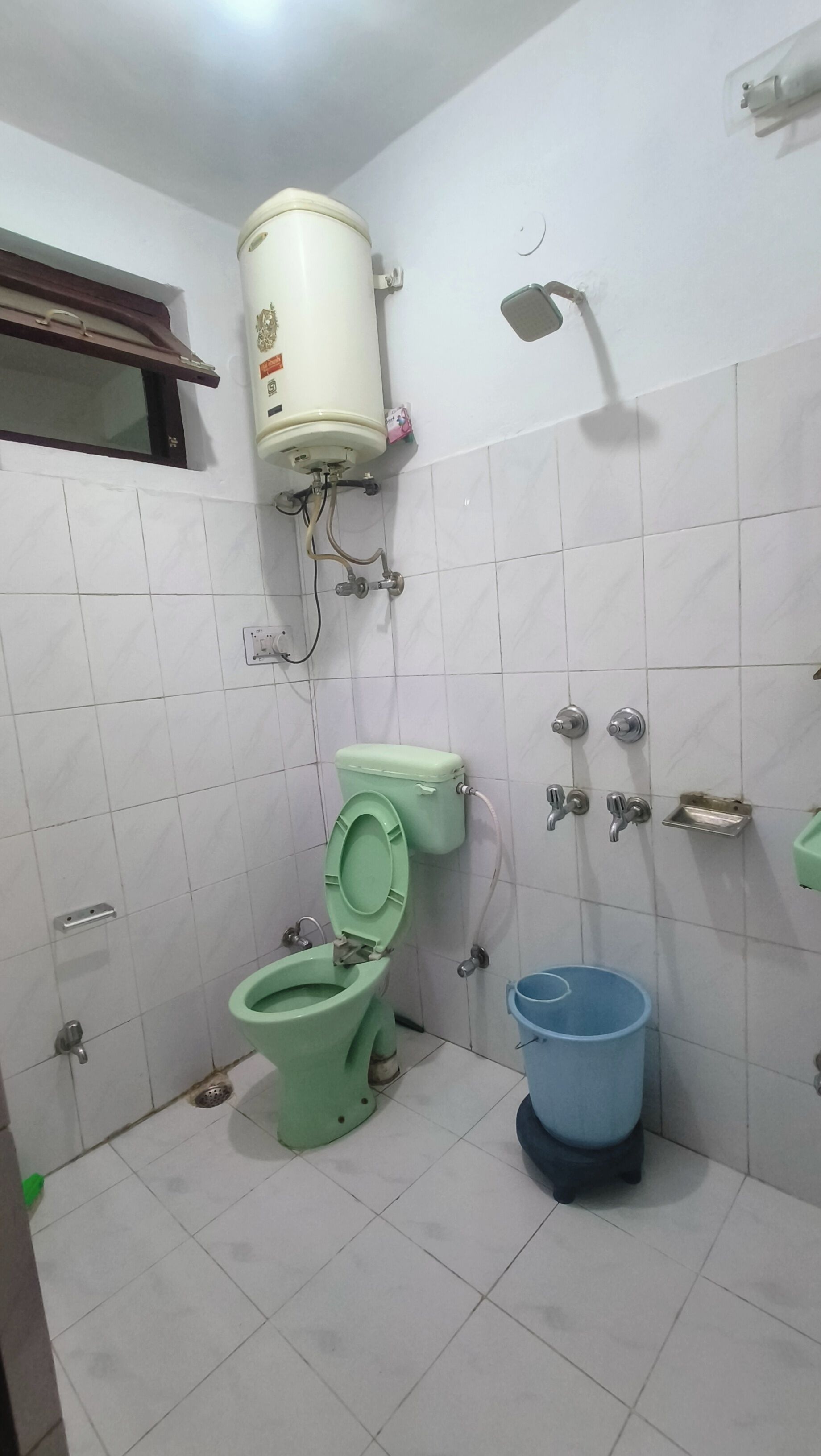 A bathroom with a green toilet, a white wall-mounted water heater, and a blue bucket.