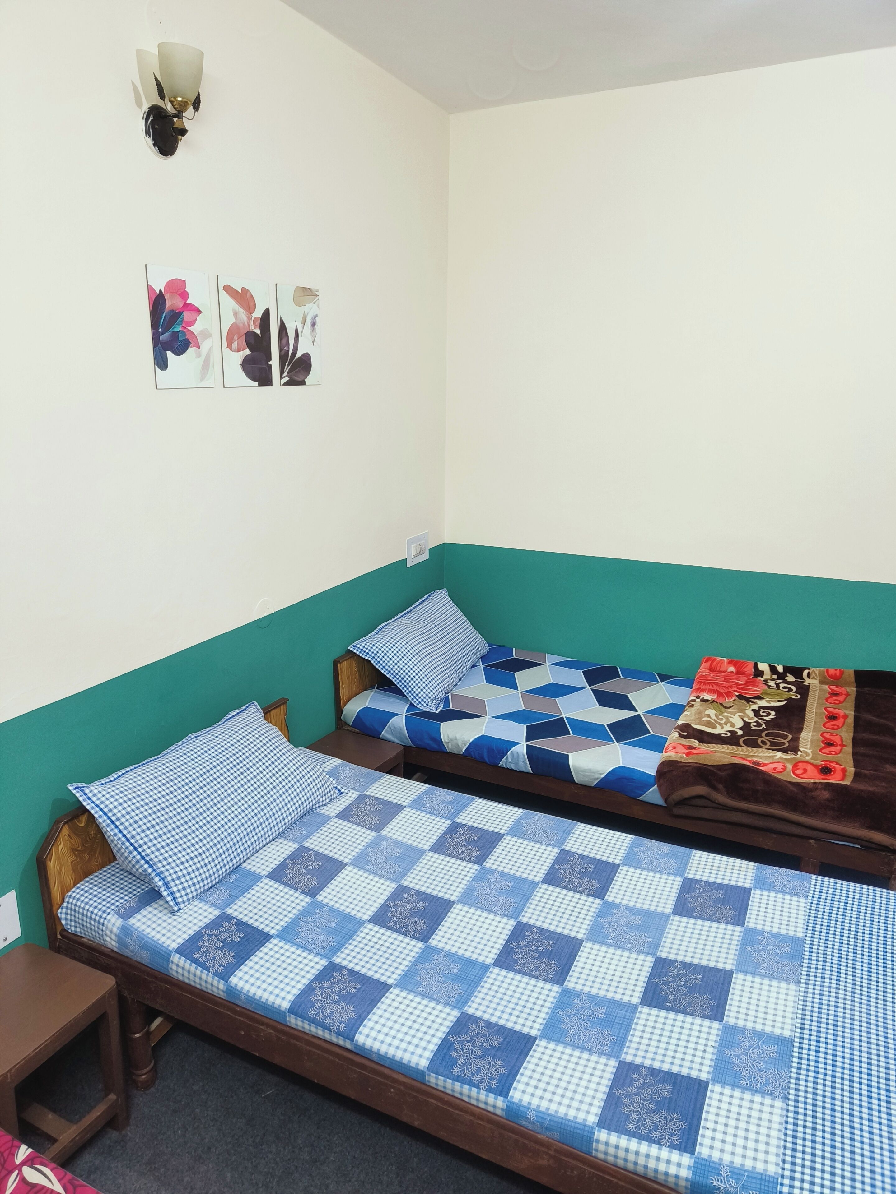 Ein kleines, ordentlich eingerichtetes Zimmer mit zwei Einzelbetten, einem kleinen Tisch und einer Wandlampe.