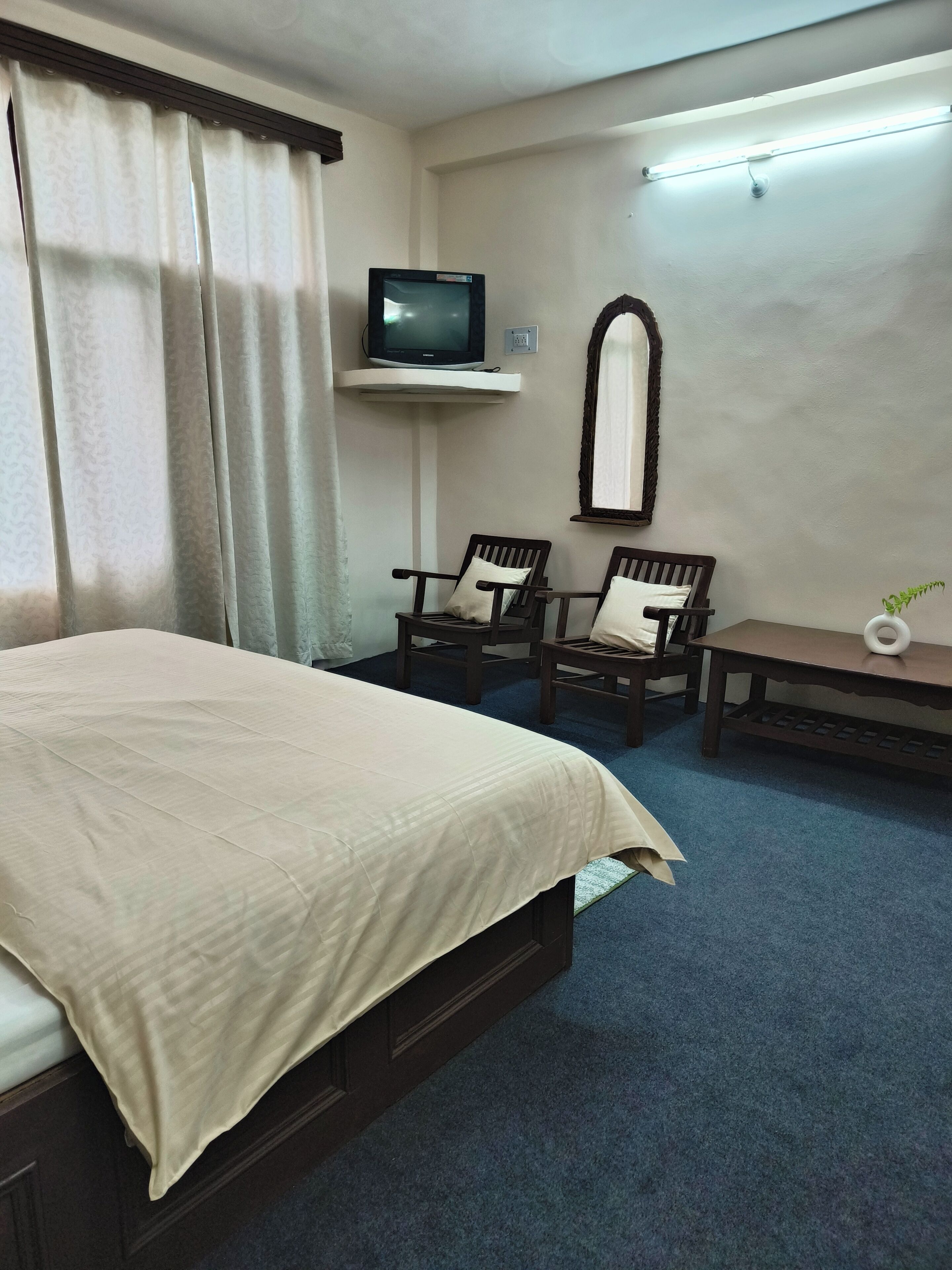 A hotel room with a bed, two chairs, a small table, a TV on a stand, and a mirror on the wall.