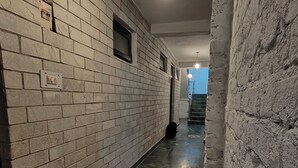 A hallway with white brick walls, a black bench, and a light fixture. - THE KAILASHA (Naggar)