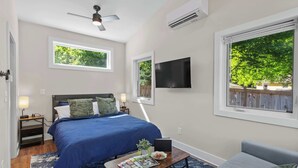 A bedroom with a bed, a desk, a chair, a TV, and large windows.