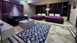Ein modernes Hotelzimmer mit einer Couch, zwei Betten, einem Couchtisch und einem gemusterten Teppich.