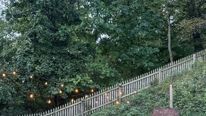 A brick outdoor seating area with a fire pit, surrounded by a wooden fence and string lights. - Spacious and Quiet 4 Bedroom House 5min Drive to DC (Arlington)