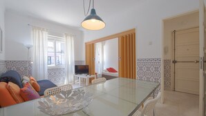 A modern kitchen with a glass dining table, white chairs, a TV, and a wooden door. - Alameda Typical by Homing (Lisbon)