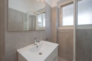 A modern bathroom with a large mirror, a white sink, and a shower area. - Alameda Typical by Homing (Lisbon)