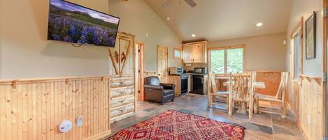 A spacious living area with a large TV, wooden paneling, a patterned rug, and a ceiling fan.