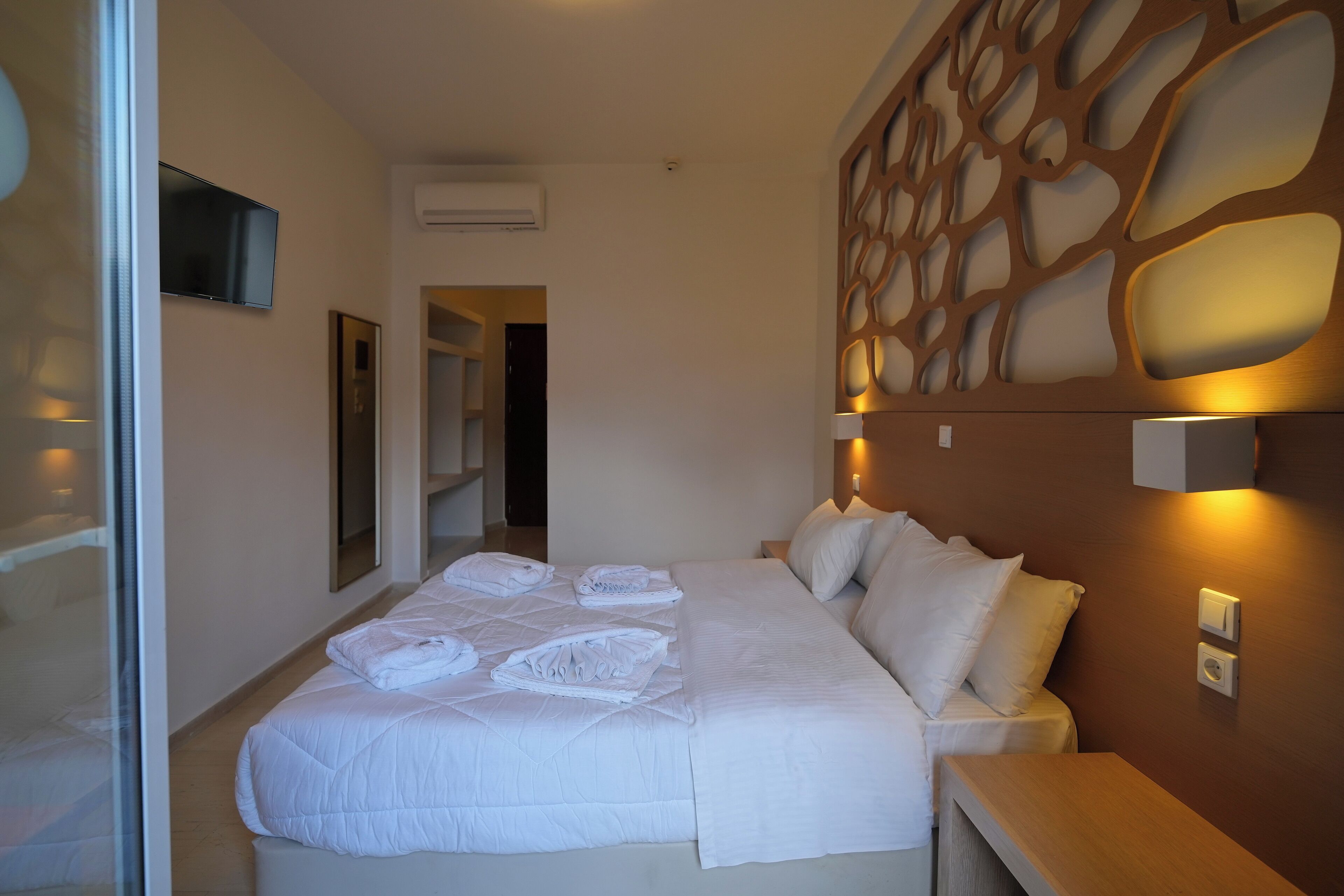 A hotel room with a large bed, a bedside table, a wall-mounted TV, and a decorative wall panel.
