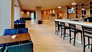 Een moderne hotellobby met een bar, zitplaatsen en een televisiescherm.