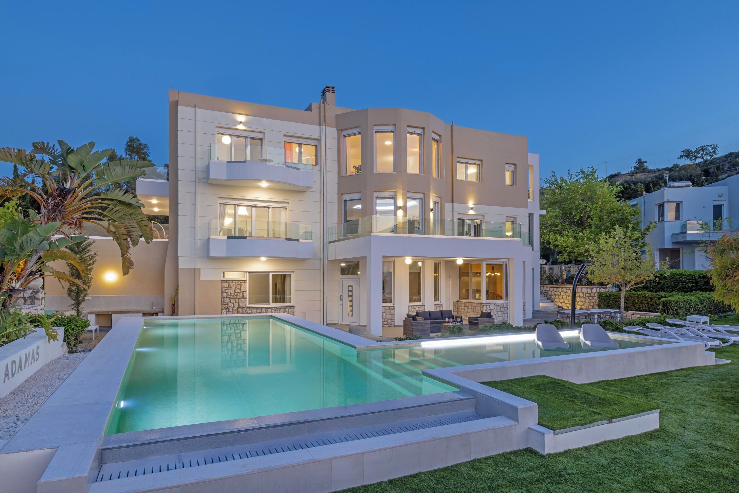 A modern multi-story house with a swimming pool, outdoor seating, and a well-maintained lawn.