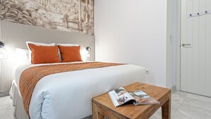 A neatly made bed with a striped headboard, two orange pillows, and a wooden nightstand with a magazine. - Genteel Home Francos VIII (Seville)