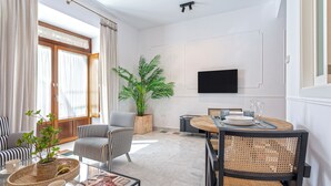 A modern living room with a dining area, featuring striped sofas, a coffee table with a magazine, a potted plant, and a flat-screen TV mounted on the wall. - Genteel Home Francos VIII (Seville)