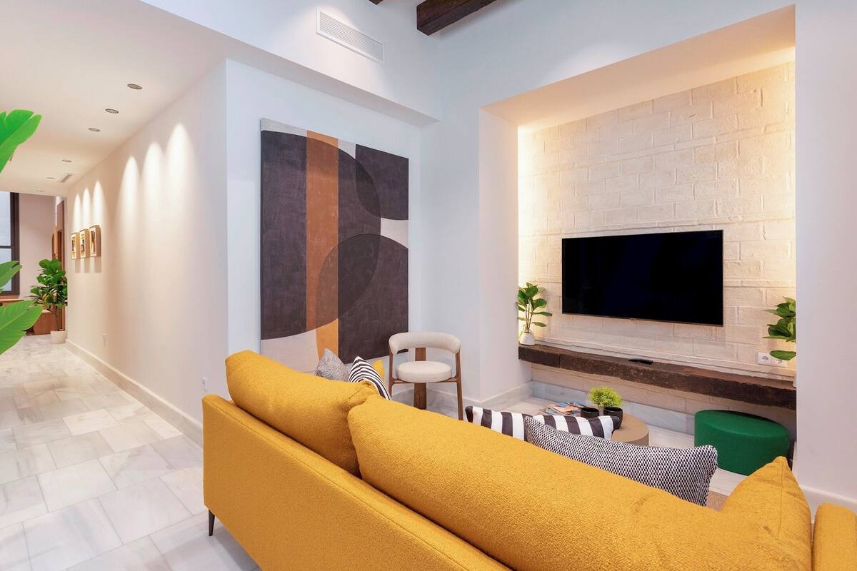A modern living room with a sofa, a flat-screen TV mounted on a brick wall, and a decorative abstract painting.