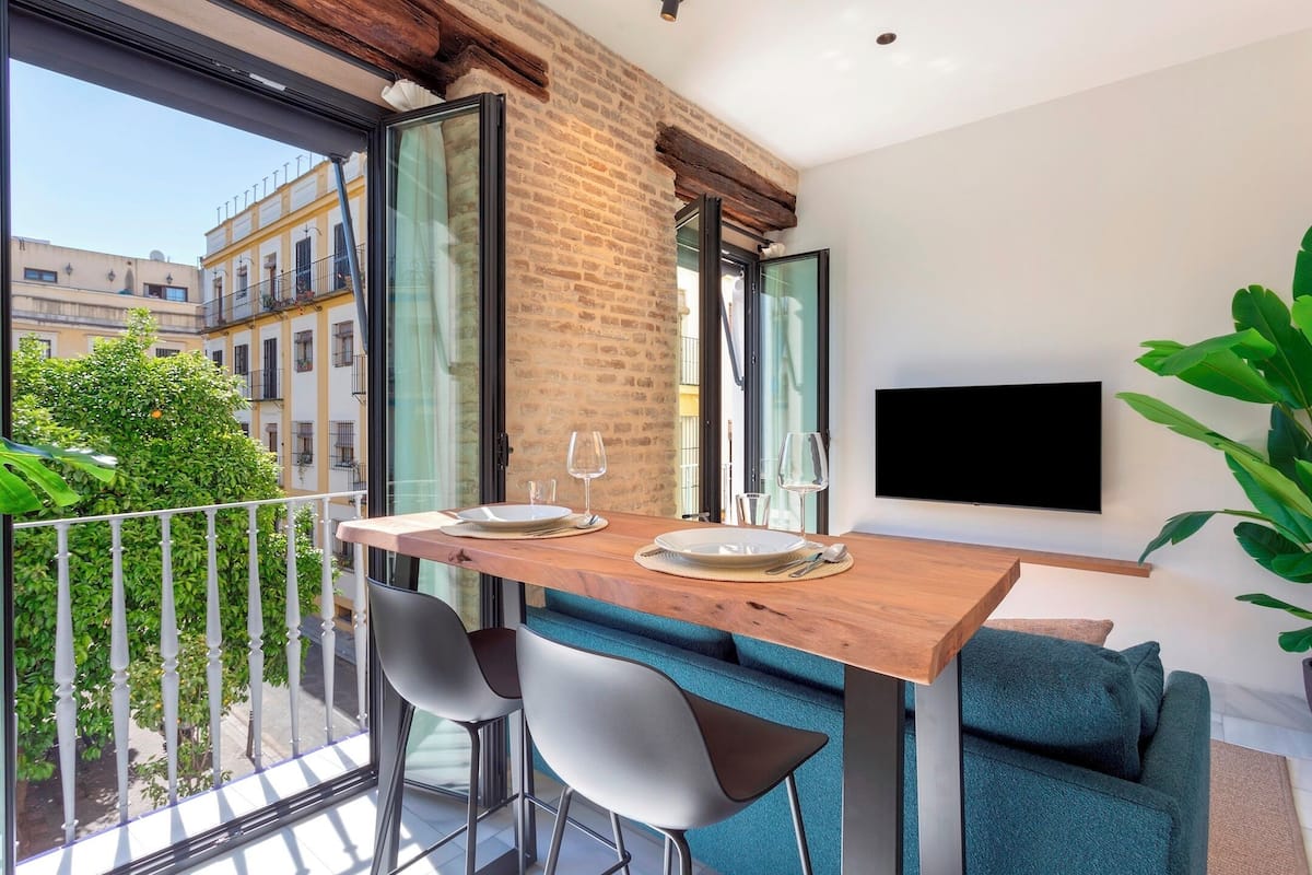 A dining area with a wooden table, two chairs, and a TV mounted on the wall.