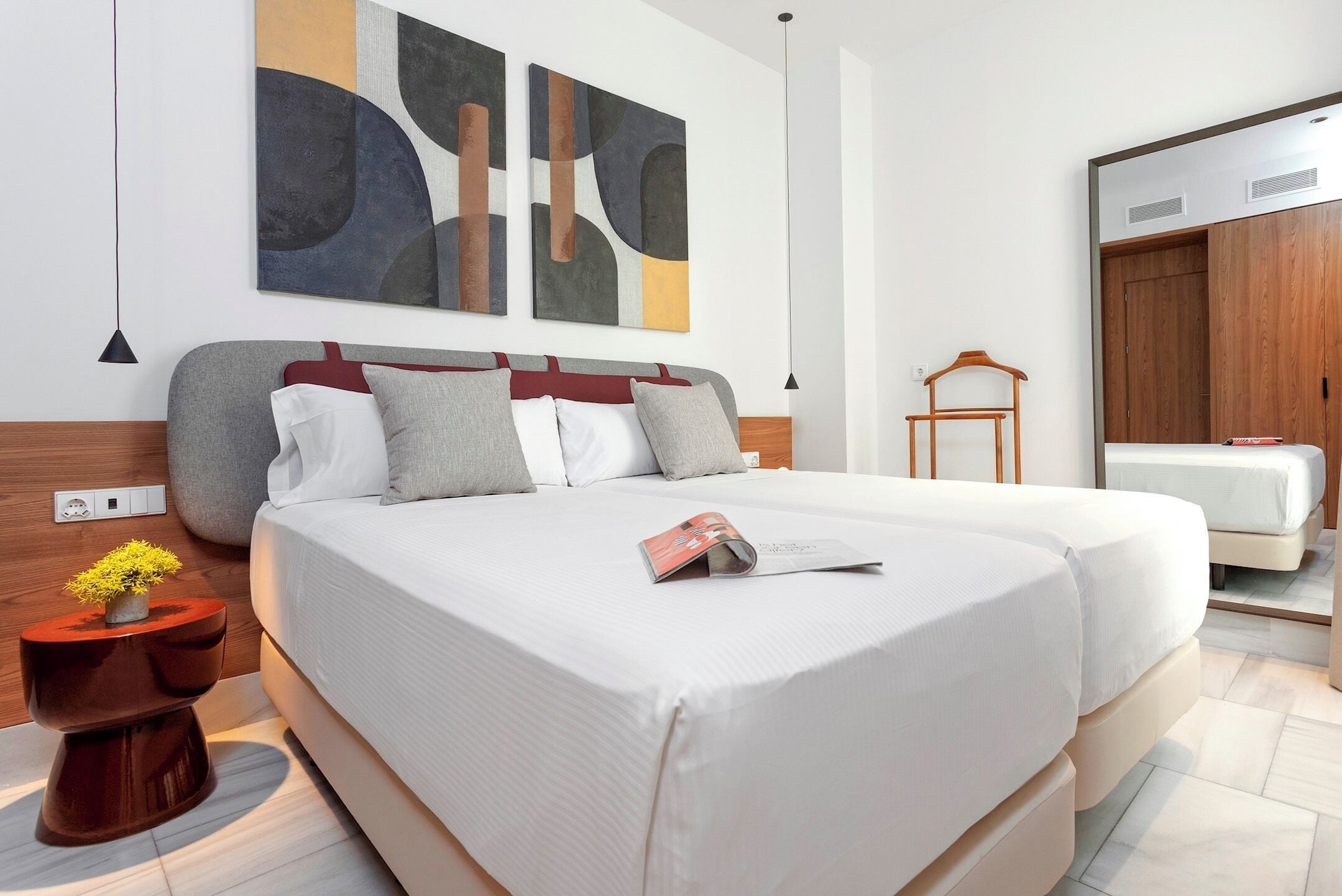 Ein modernes Hotelzimmer mit einem großen Bett, einem Nachttisch mit Pflanze, einem Kleiderschrank und abstrakter Wandkunst.