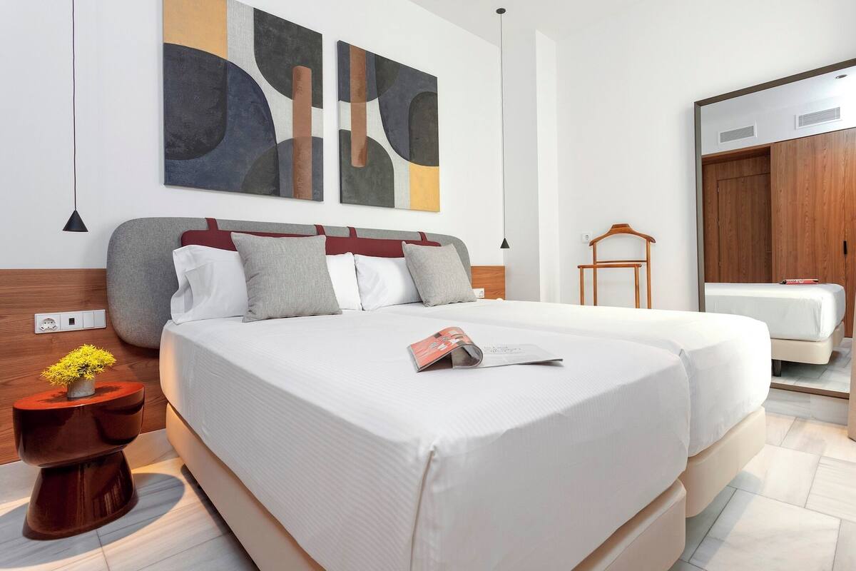 A modern hotel room with a large bed, a wooden wardrobe, and abstract wall art.