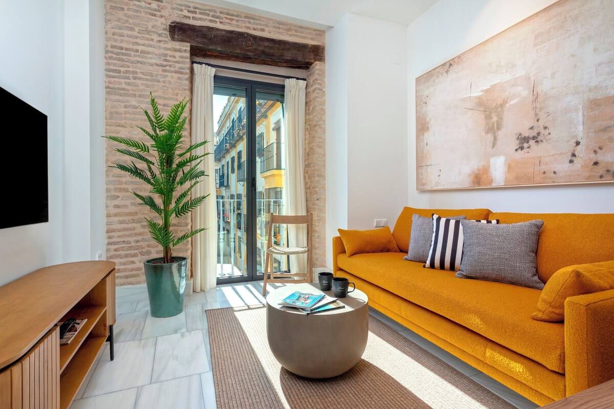 A modern living room with a brick wall, a large window, a sofa, a coffee table, and a potted plant.