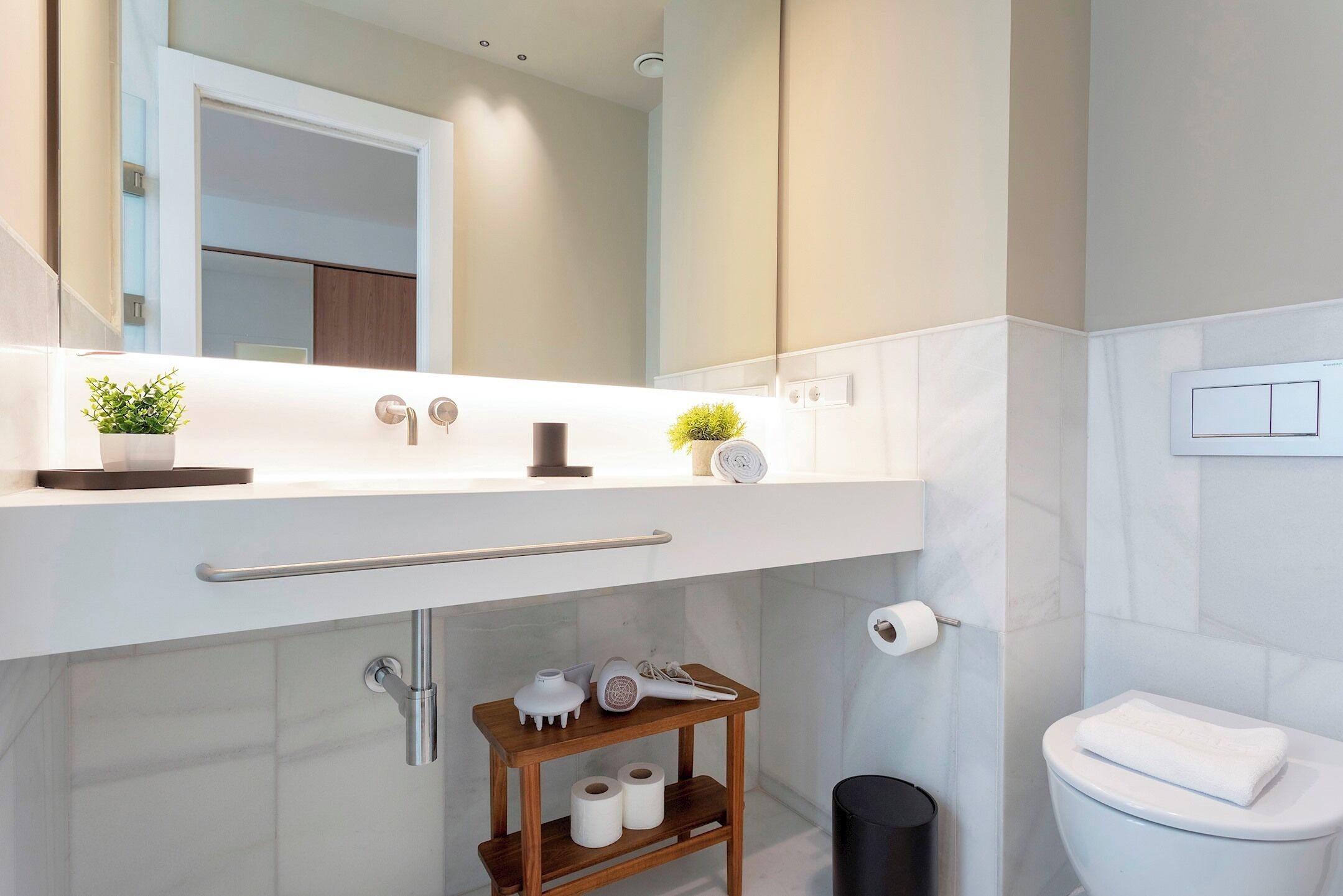 Une salle de bain moderne avec un meuble-lavabo blanc, un miroir, une petite étagère contenant des articles de toilette et des toilettes.
