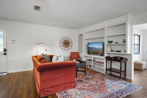 A living room with a red sofa, a patterned rug, a TV on a stand, and a bookshelf.