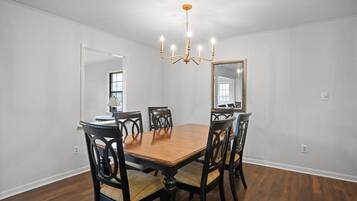 Une salle à manger avec une table et des chaises en bois, un lustre et un grand miroir au mur.
