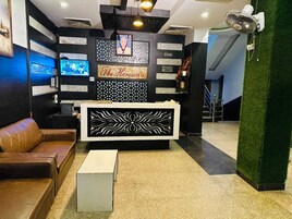 Un área de recepción con diseño moderno, que incluye un mostrador de recepción, un sofá de cuero marrón, una mesita blanca y una pantalla de televisión mostrando un programa.