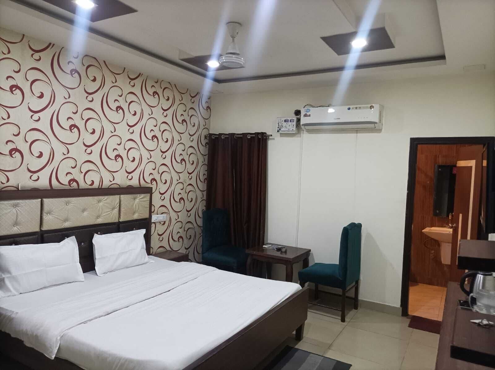 Habitación de hotel con cama, escritorio, silla, equipo de aire acondicionado y baño con lavamanos.